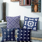 Four blue patterned pillows on a gray sofa with a decorative wall in the background.