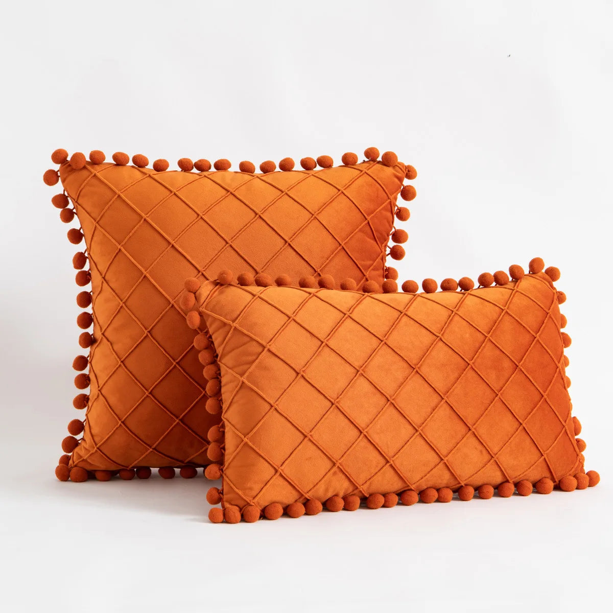 Two orange textured pillows with pom-pom trim on a white background