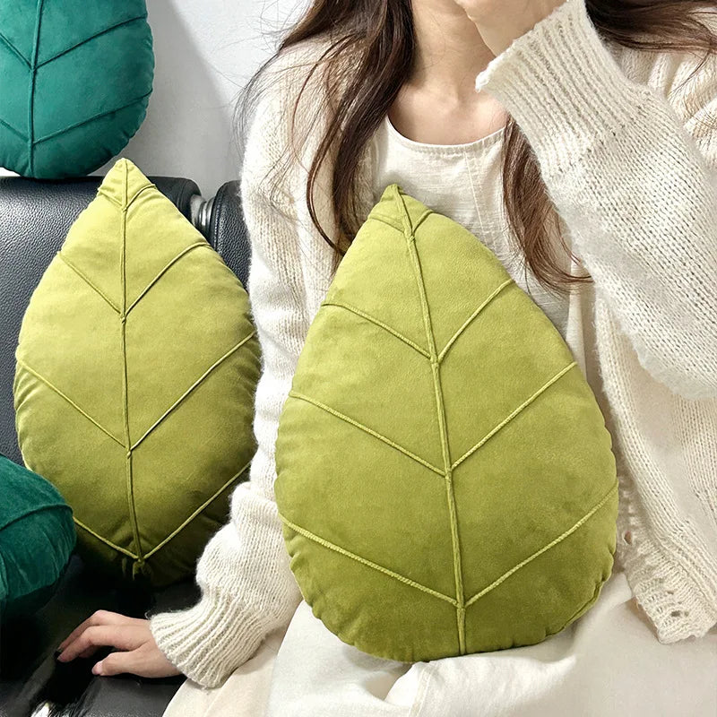 Person holding a green leaf-shaped pillow with a white sweater.