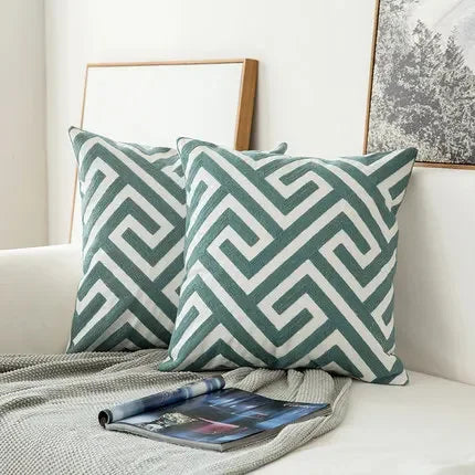 Two green and white patterned pillows on a couch with a magazine underneath.