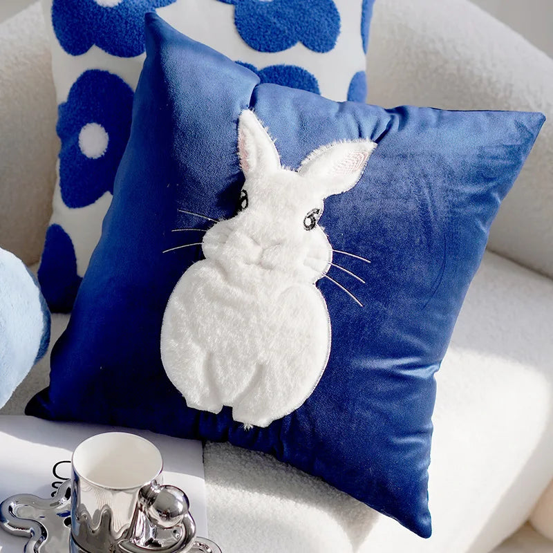 Blue pillow with a white rabbit design on a white couch with floral cushions.