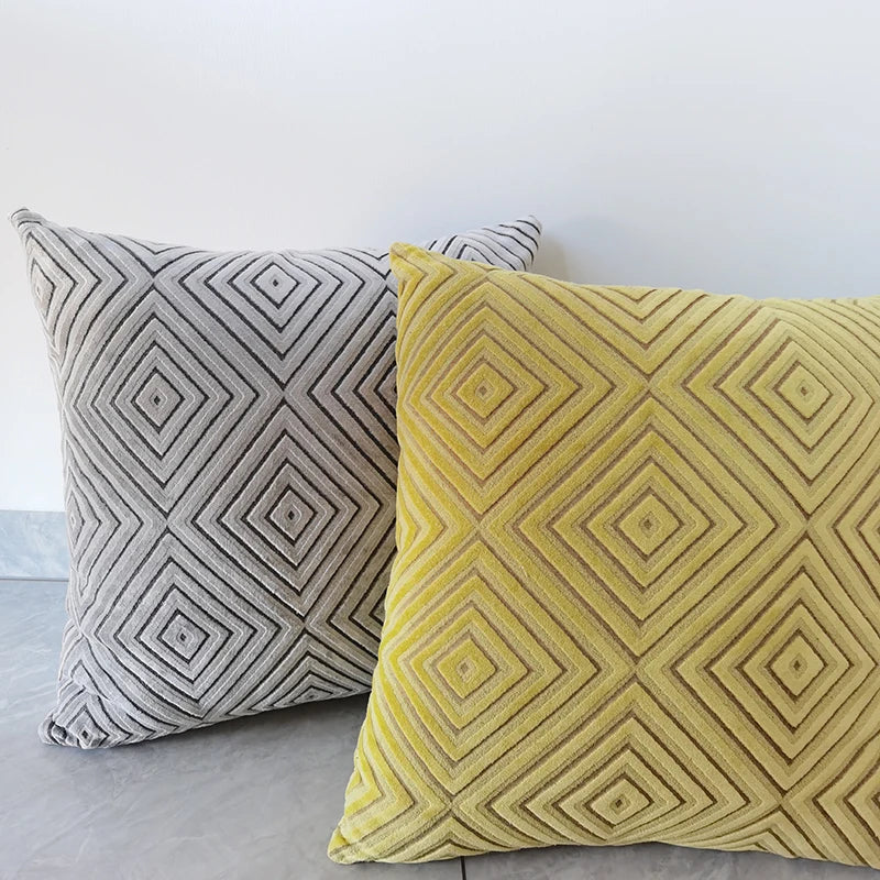 Two patterned pillows, one gray and one yellow, on a light gray surface.