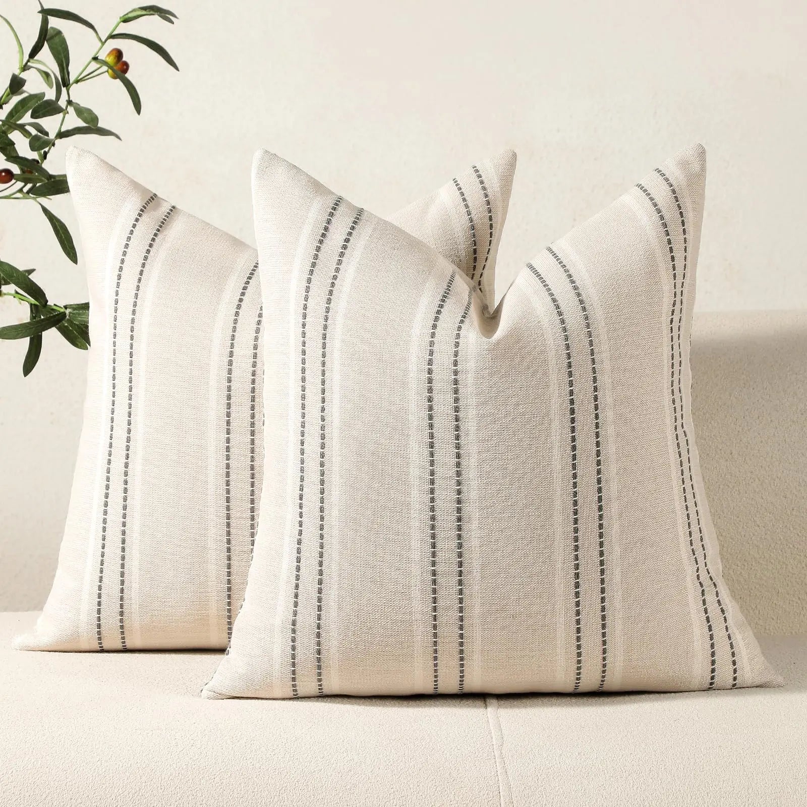 Two beige pillows with black stripes on a light-colored couch, with a plant in the background.