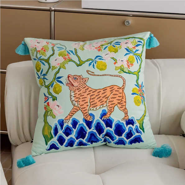 Decorative pillow with a tiger design on a light blue background, featuring tassels, on a beige sofa.