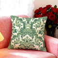 Green patterned pillow on a pink couch with red flowers in the background