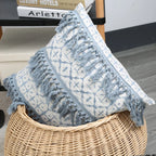 Decorative pillow with blue tassels in a wicker basket on a wooden floor.