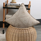 Decorative pillow with geometric pattern on a wicker stool in a room setting.
