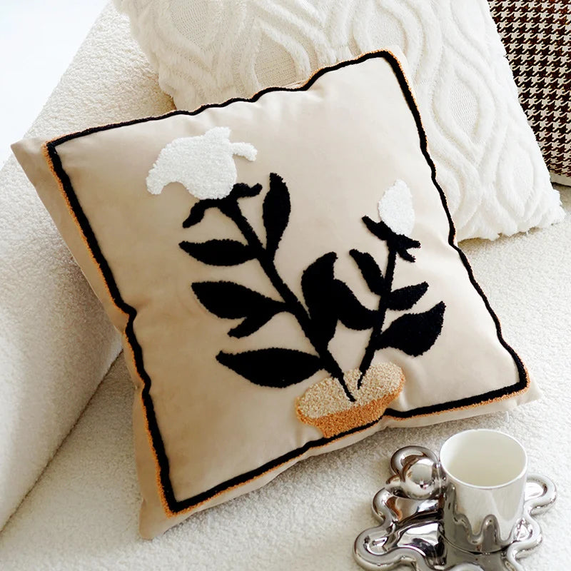 Decorative pillow with black floral design on a white surface with a cup and saucer.