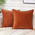 Two orange pillows on a bed with a neutral background