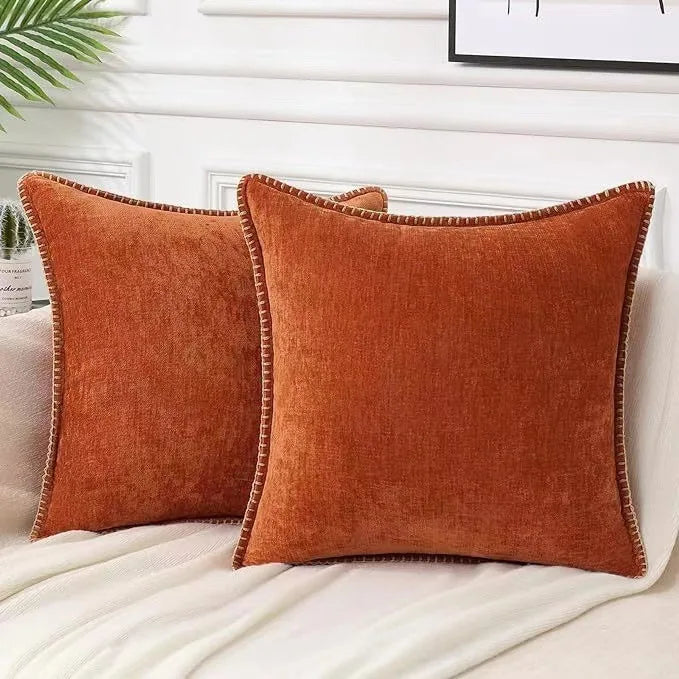 Two orange pillows on a bed with a neutral background