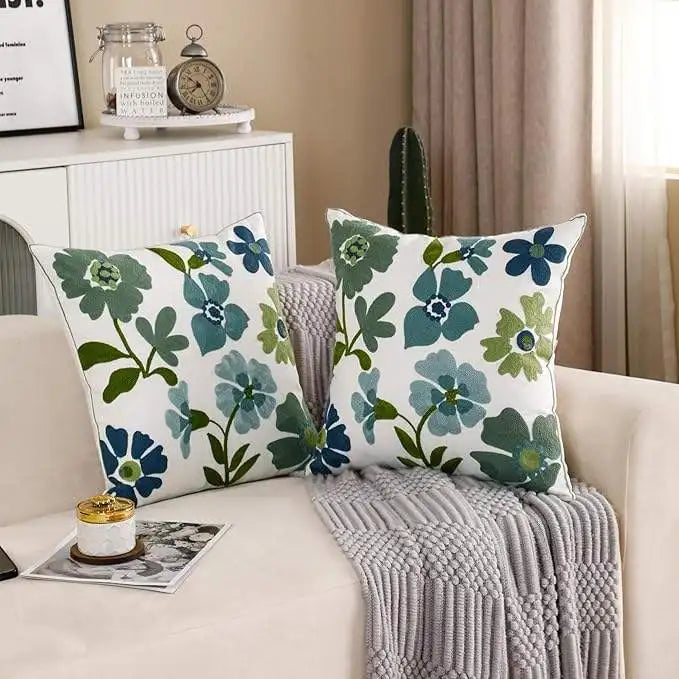 Floral-patterned pillows on a couch with a side table and decor items in the background.