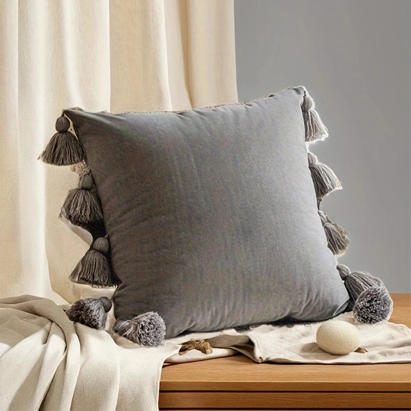 Gray pillow with tassels on a wooden surface with neutral background