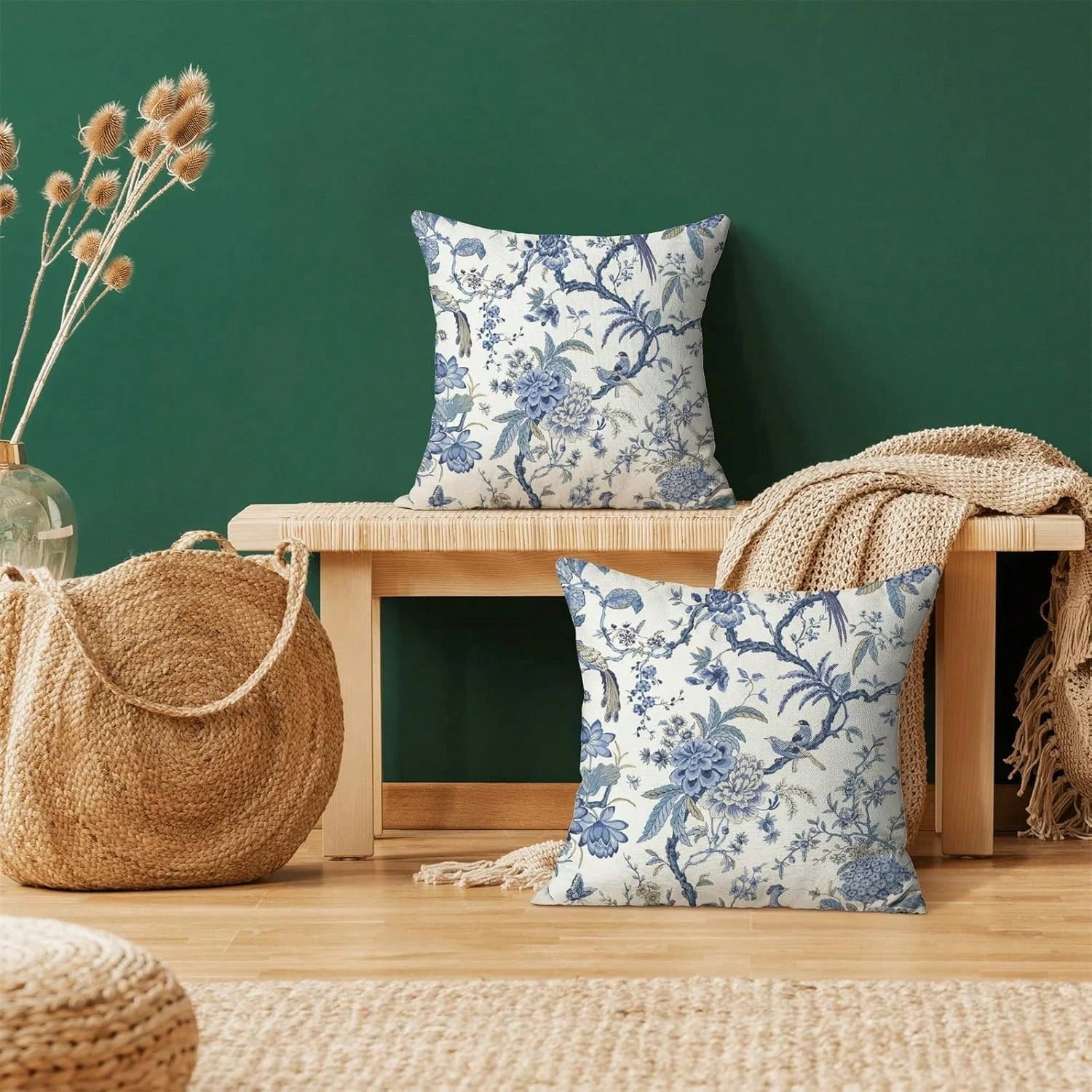 Floral-patterned pillows on a wooden bench against a green wall with a woven bag and decorative elements.
