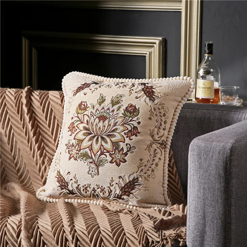 Decorative pillow with floral pattern on a couch next to a table with a bottle and glass.