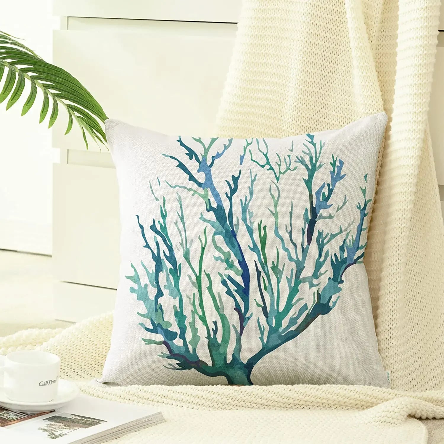 Decorative pillow with blue and green coral design on a white background, placed on a couch.
