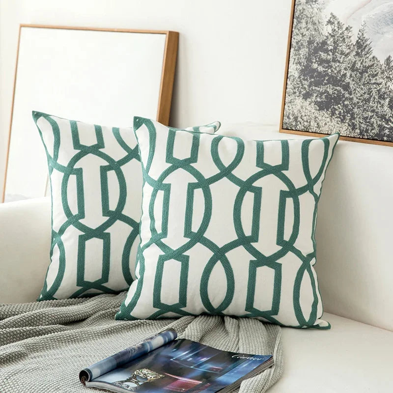 Two green and white patterned pillows on a couch with a magazine underneath.