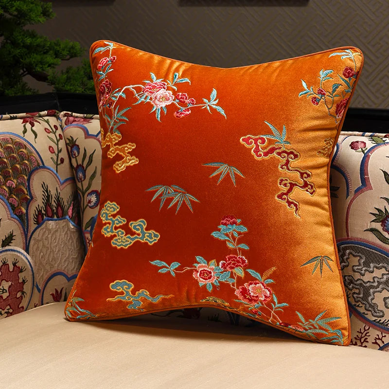 Decorative orange pillow with floral embroidery on a patterned sofa.