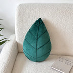 Teal leaf-shaped pillow on a beige sofa with a white wall background