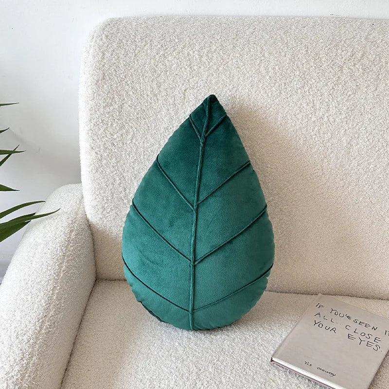 Teal leaf-shaped pillow on a beige sofa with a white wall background
