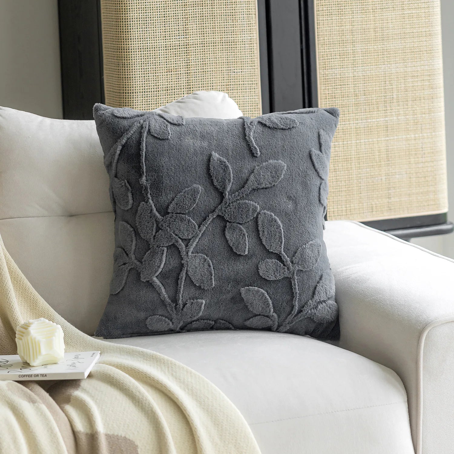 Gray decorative pillow with leaf pattern on a beige sofa.