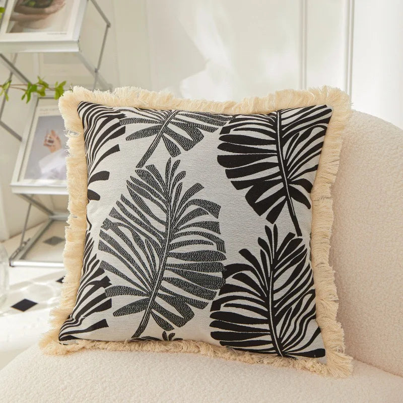Decorative pillow with black leaf pattern on a white background, placed on a sofa.