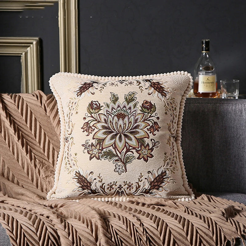 Decorative pillow with floral pattern on a textured surface, with a bottle and glasses in the background.