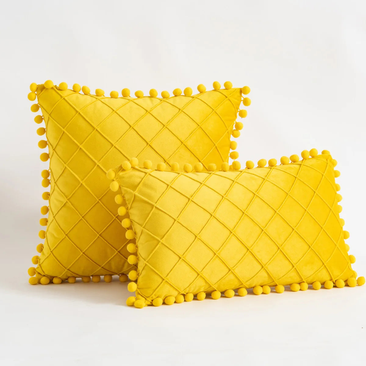 Two yellow textured pillows with pom-pom trim on a white background