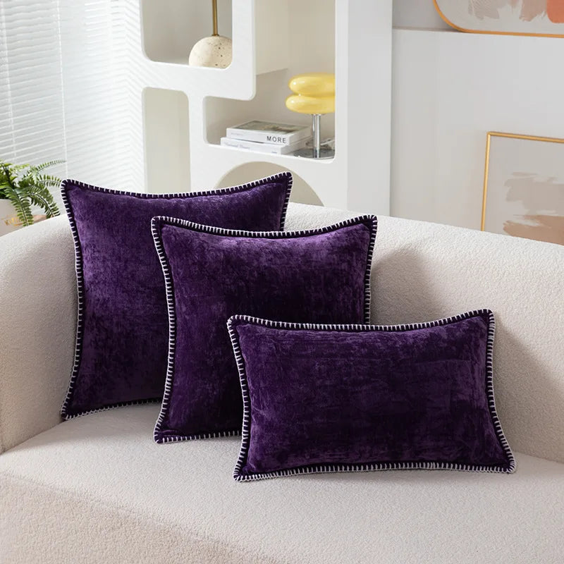 Three purple pillows with black trim on a white couch in a living room setting.