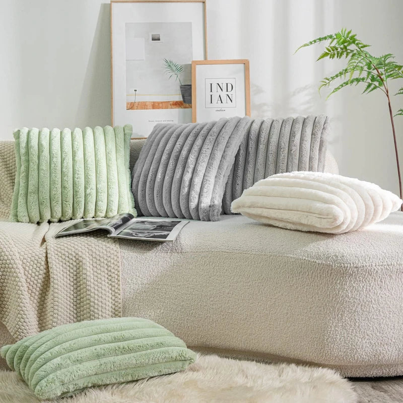Beige sofa with green, gray, and white textured pillows in a living room setting.