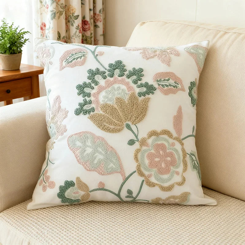 Decorative floral pillow on a beige sofa with a plant and curtain in the background
