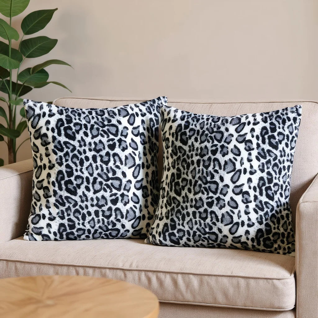 Two leopard print pillows on a beige sofa with a plant in the background.