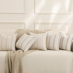 Beige sofa with striped cushions and a blanket against a white paneled wall.