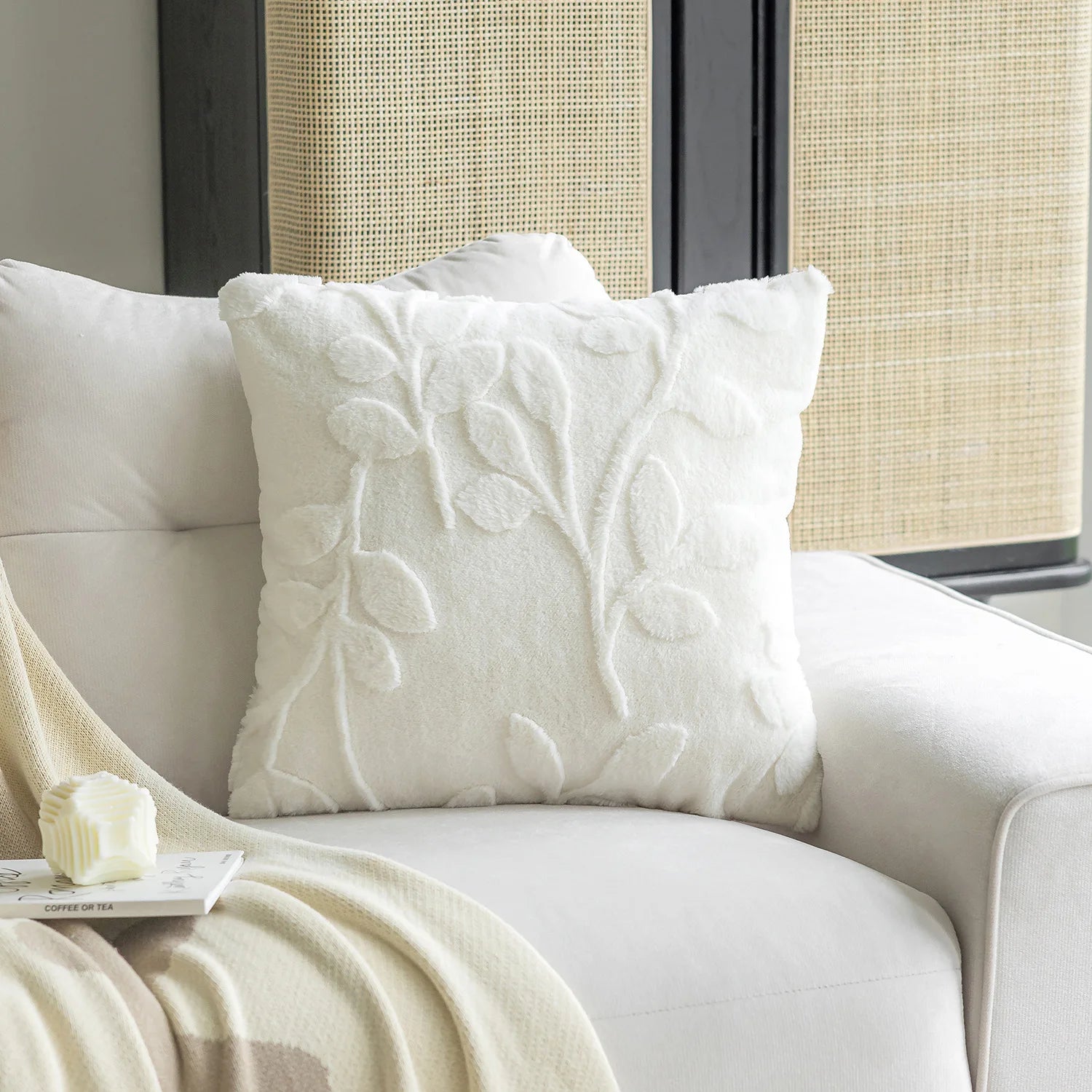 White textured pillow on a beige armchair with a blanket and small object in the foreground.