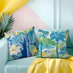 Tropical patterned pillows on a light blue sofa with a yellow blanket and leaf decoration.