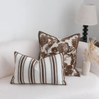Two decorative pillows on a white couch with a lamp in the background.