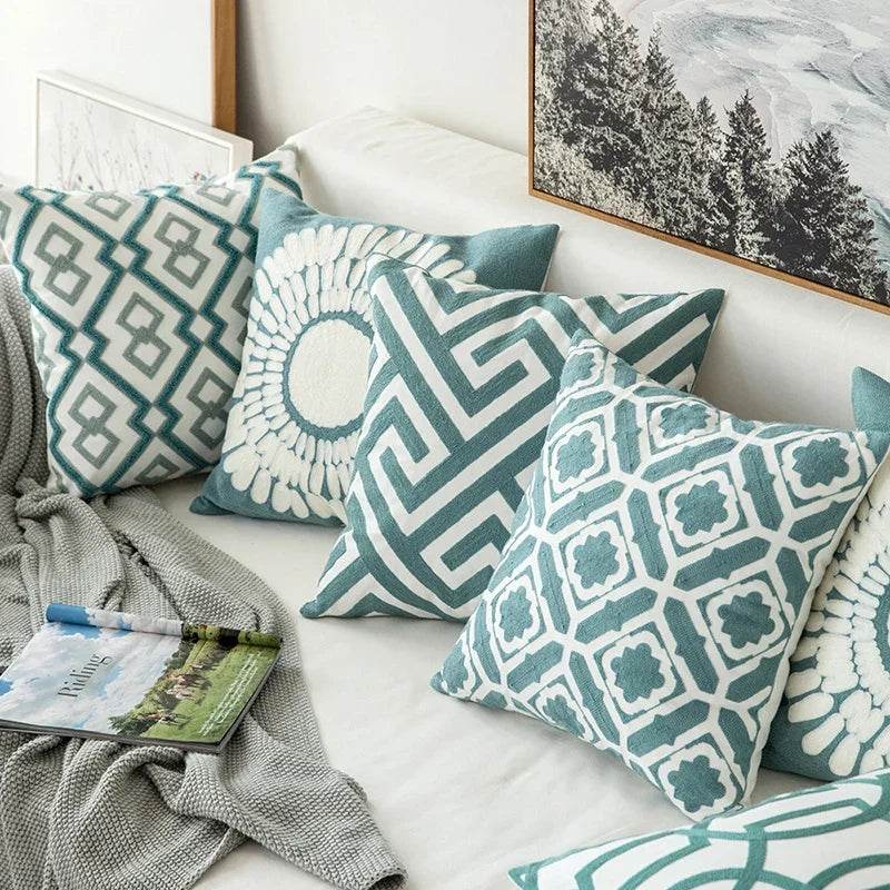 Patterned teal and white cushions on a sofa with a magazine and blanket.