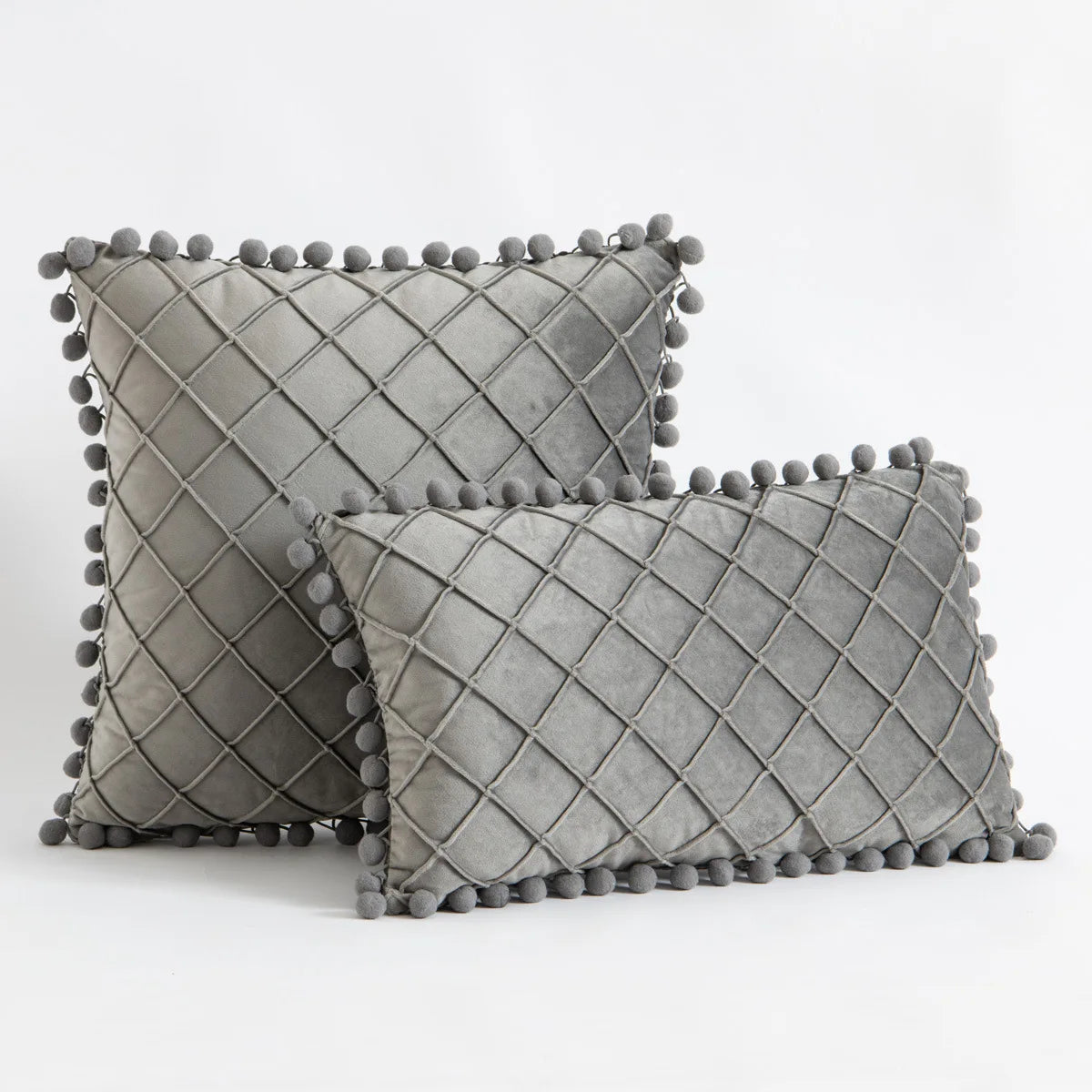Two gray textured pillows with pom-pom details on a light gray background