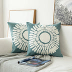 Two blue pillows with white patterns on a white couch with a blanket and magazine.